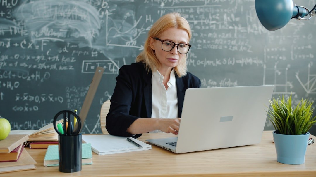Teacher working on a laptop at a desk in a classroom