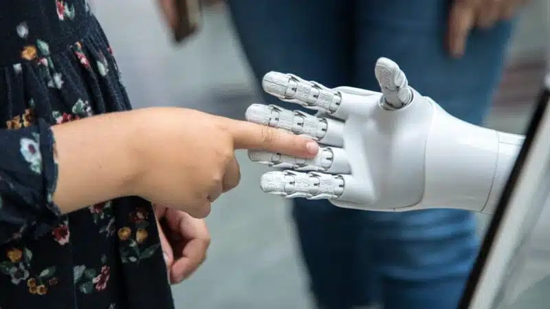 A child touching the finger of a white robotic hand, representing trust and boundaries in AI systems