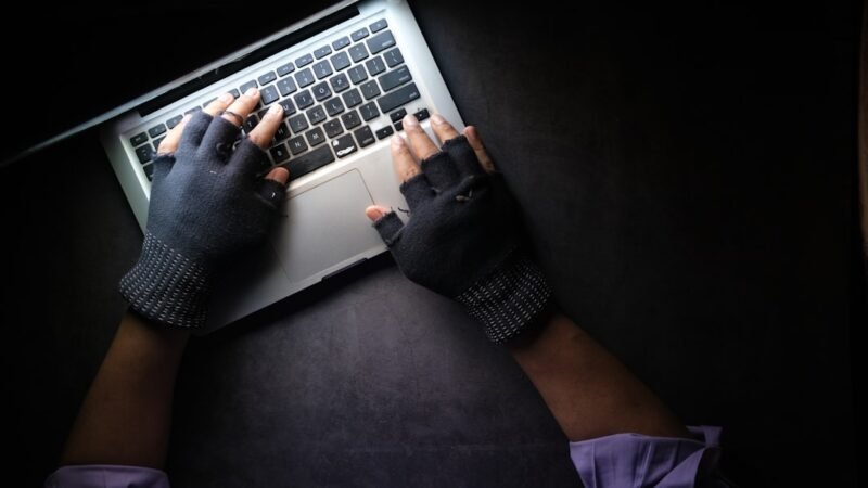 A hand reaching toward a laptop keyboard, representing the risk of ClickFix malware attacks tricking users