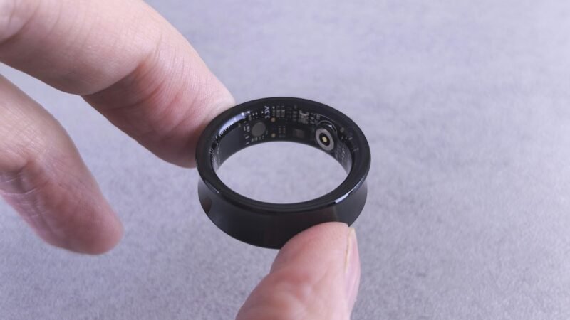 Closeup of fingers holding a black smart ring with visible circuits