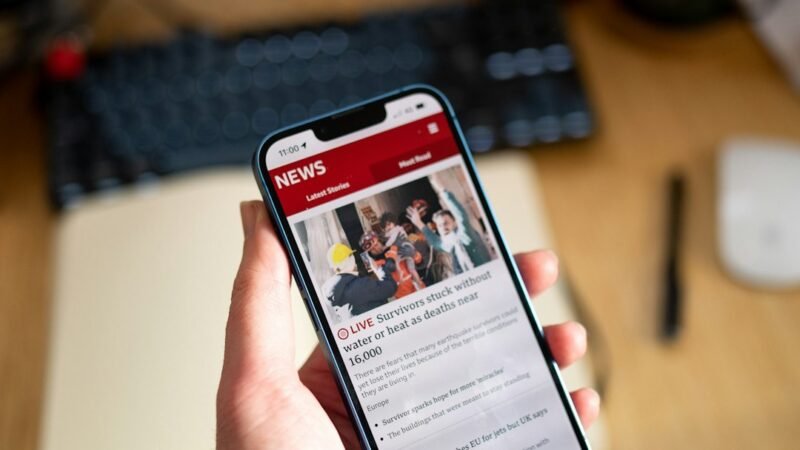 A hand holding a phone while browsing current events news stories, illustrating Google Discover's new AI summary feature