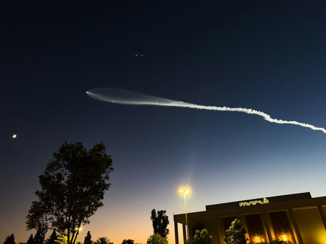 Rocket exhaust trail streaking across the night sky above city buildings