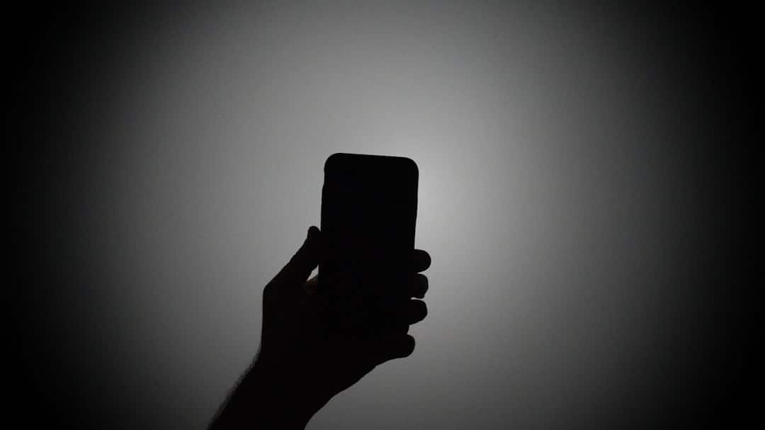 Silhouette of a hand holding a smartphone with the screen lit up