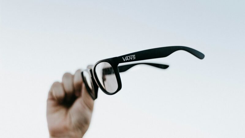 Close up of a person holding a pair of smart glasses with a camera lens built into the frame