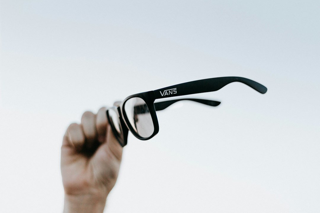 Close up of a person holding a pair of smart glasses with a camera lens built into the frame
