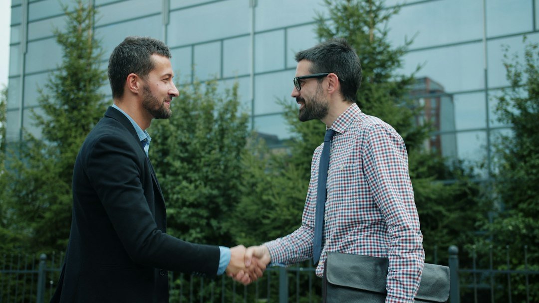 Two businessmen shaking hands outdoors, representing the Thrive Holdings and ADT acquisition deal