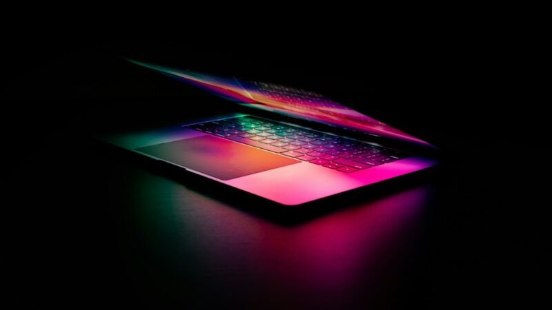 A laptop keyboard glowing with pink and green light, representing AI search technology