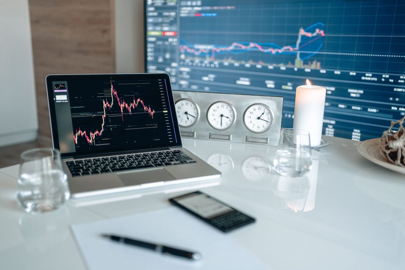 Laptop showing a stock chart in front of a large market data display