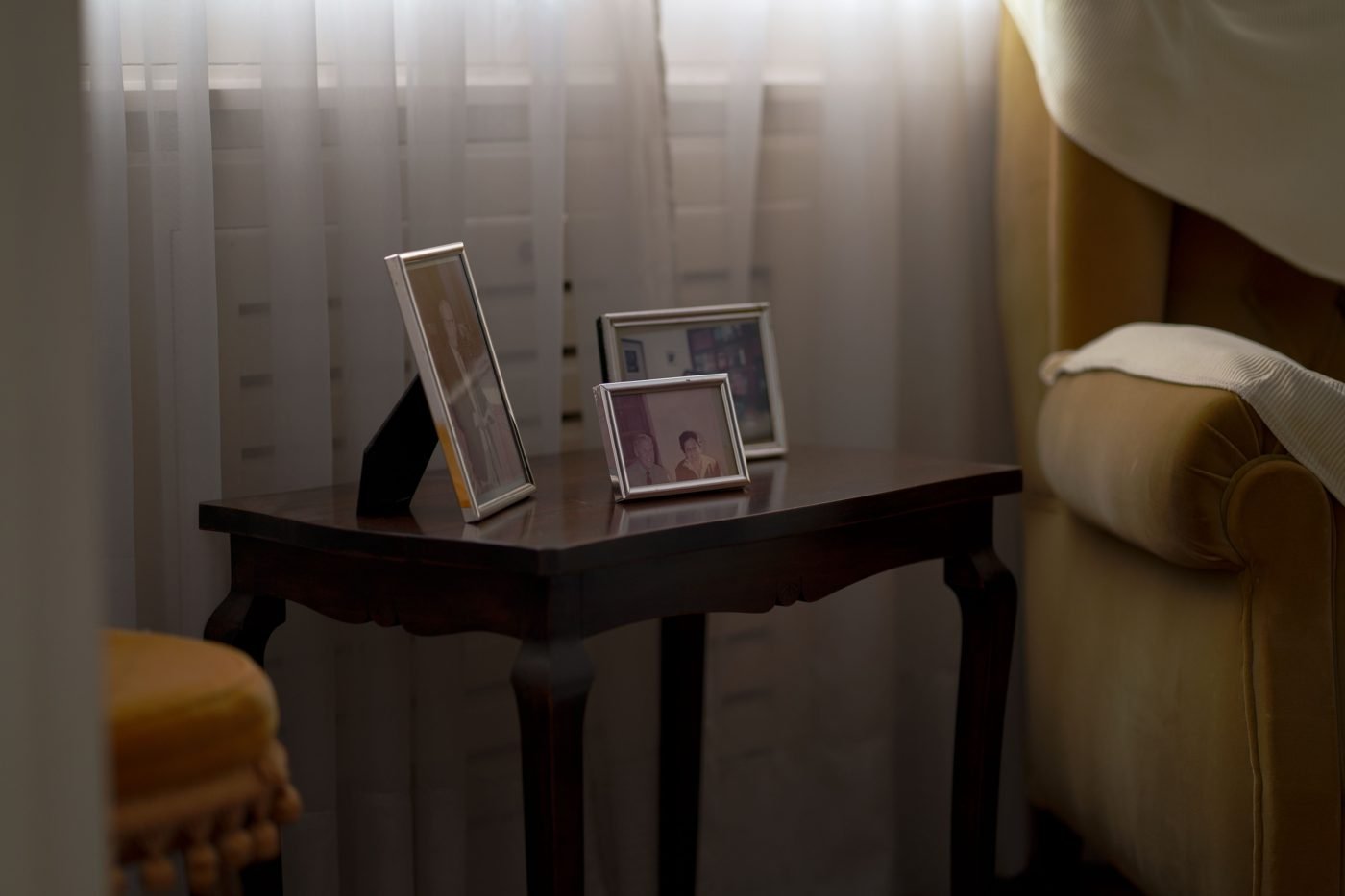 Framed photos on a table in a cozy living room corner near a window