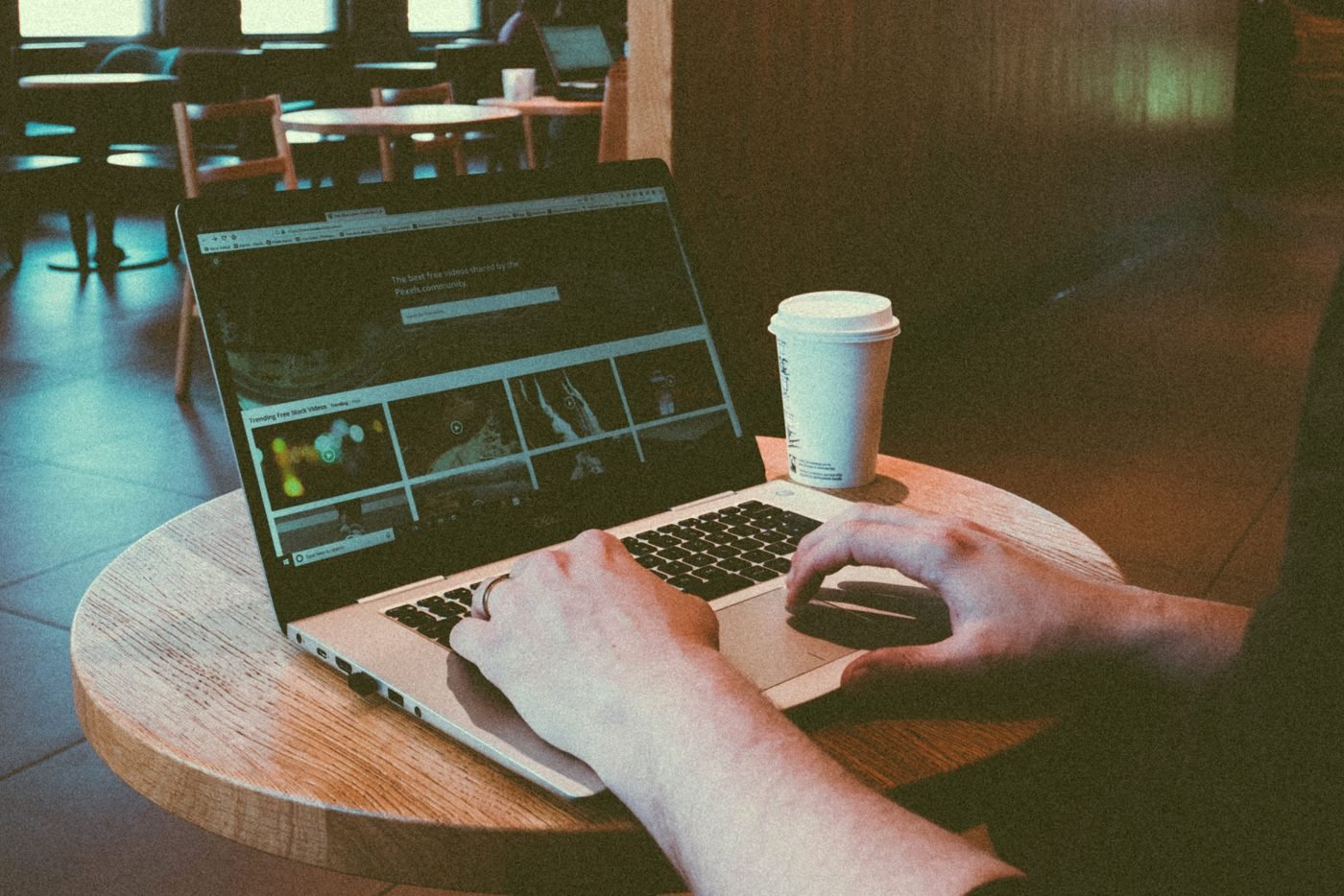 A person using a laptop at a round wooden cafe table