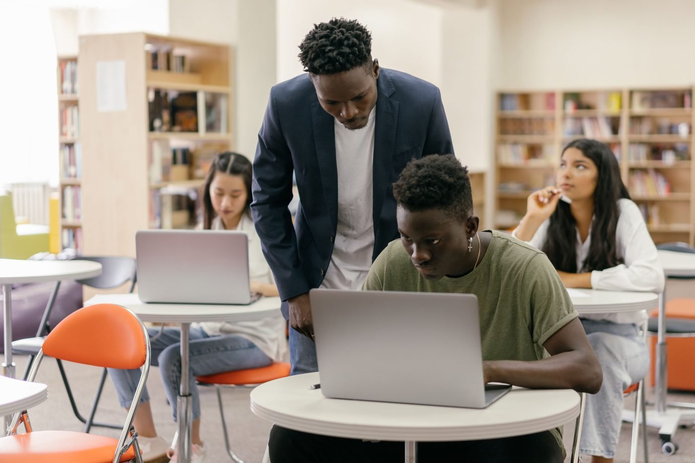 Teacher helping students working on laptops in a classroom