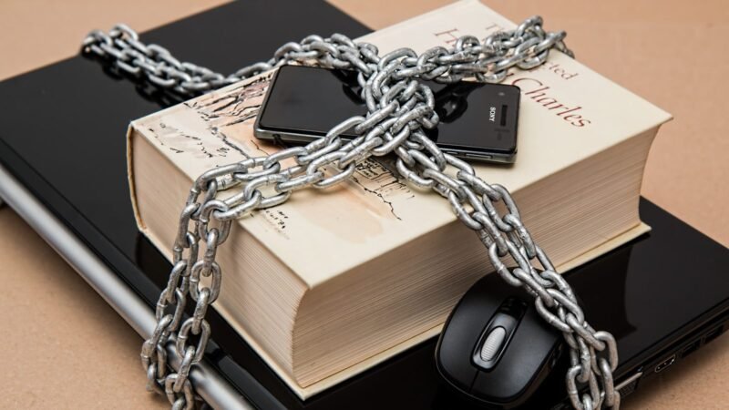 Book, phone and laptop wrapped in a metal chain with a padlock, symbolizing data security