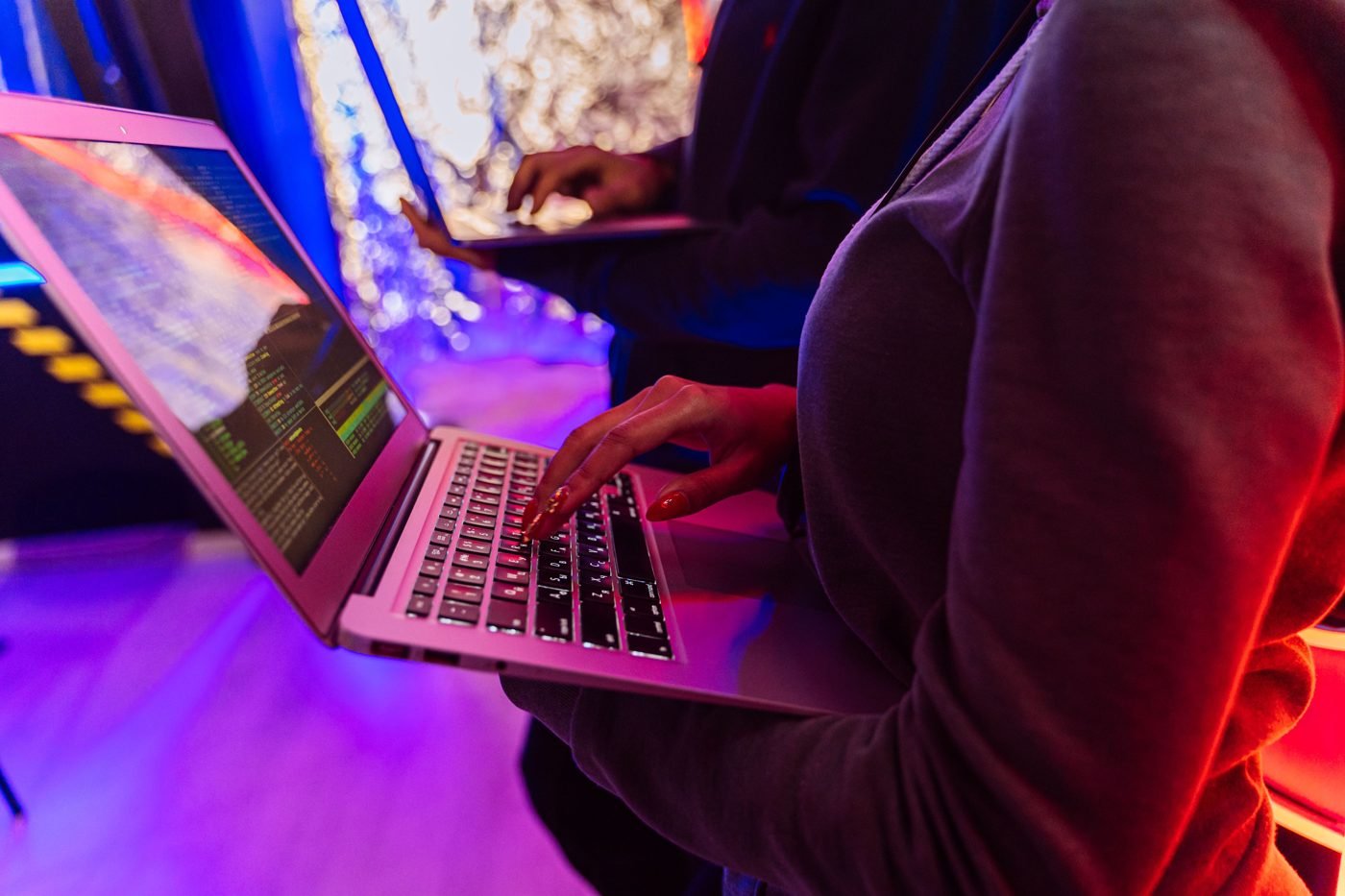 People working on laptops in a dim room lit by colorful lights