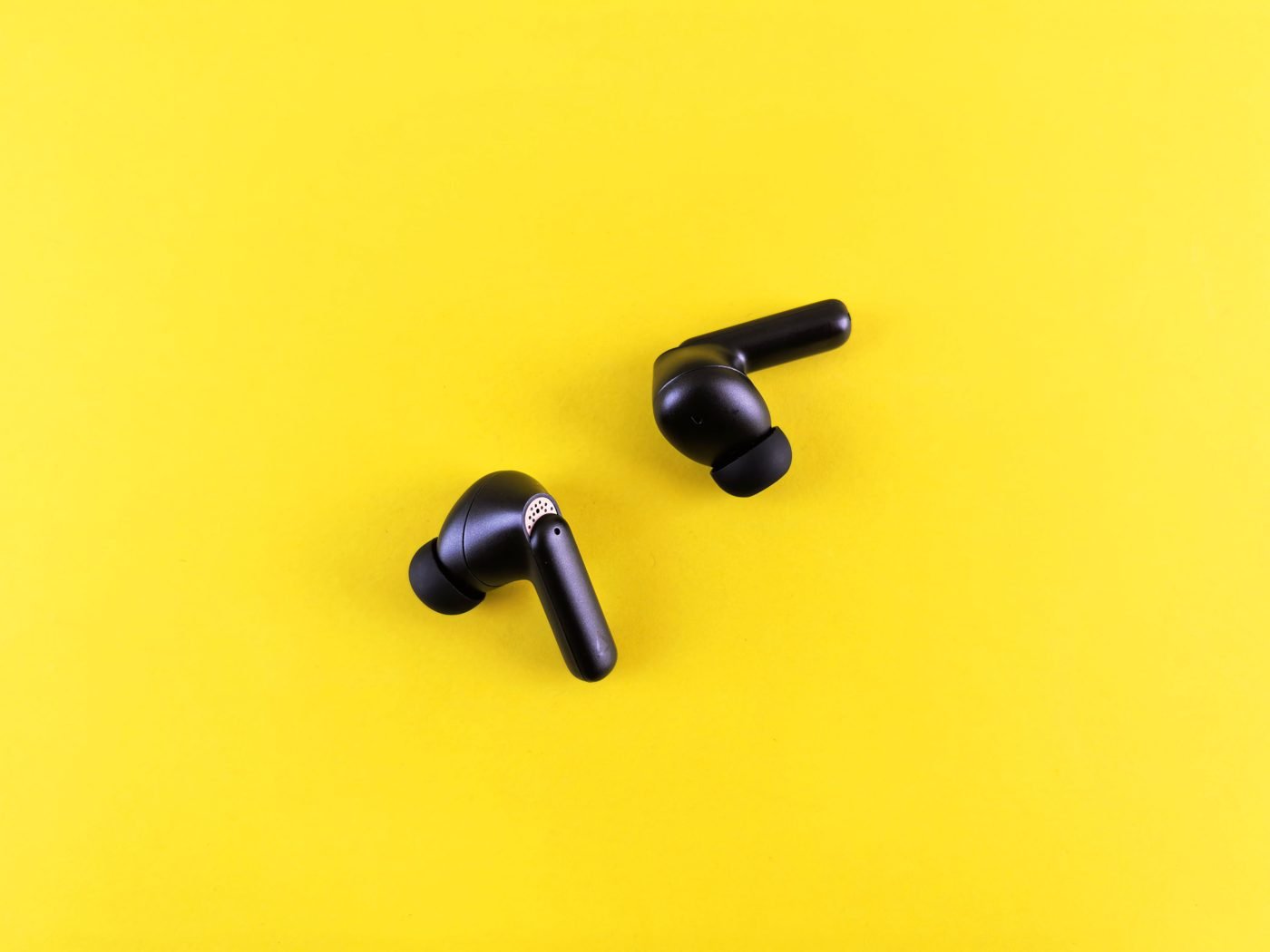 Black wireless earbuds on a bright yellow background