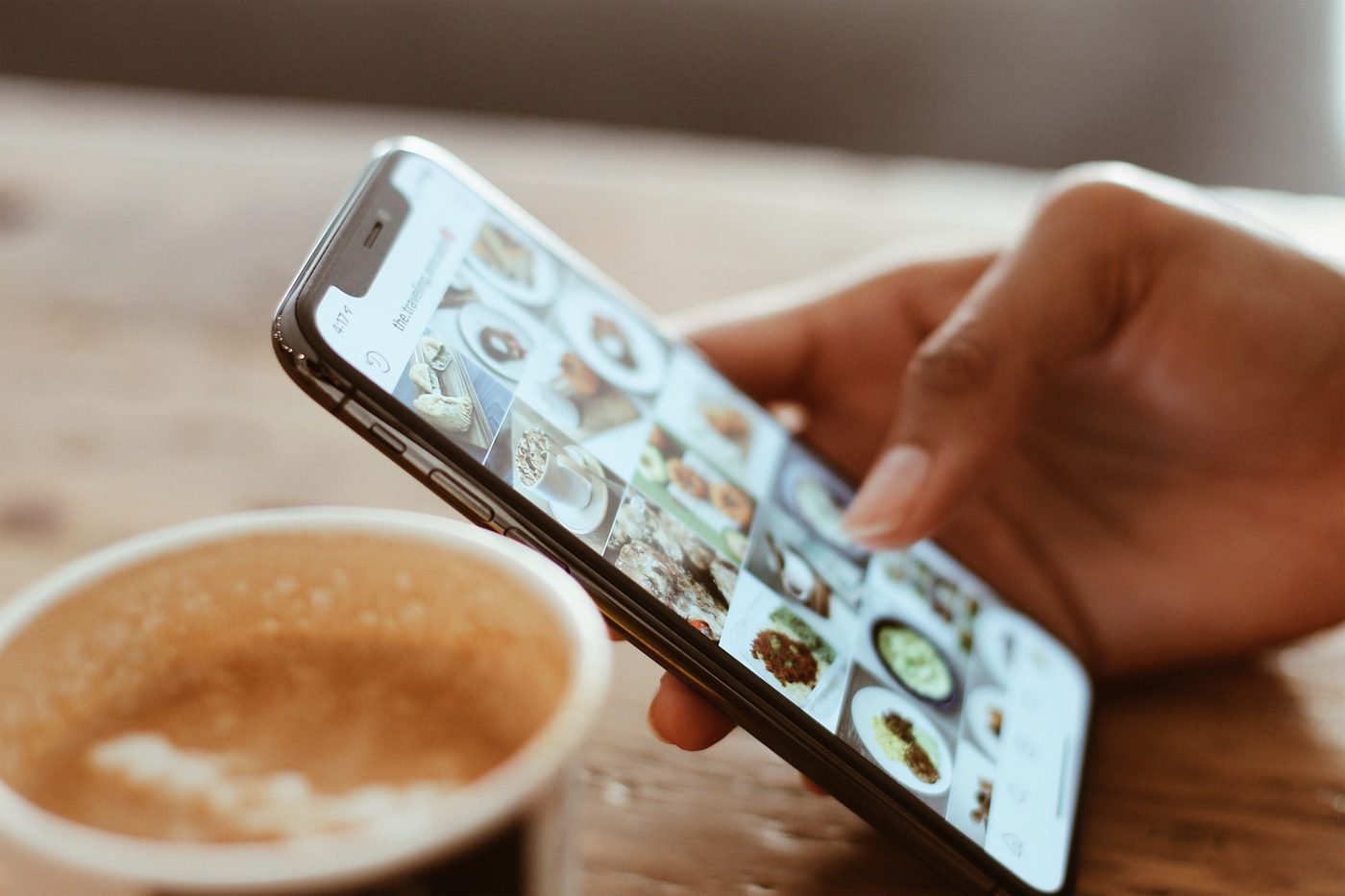 Hand scrolling a smartphone next to a cup of coffee
