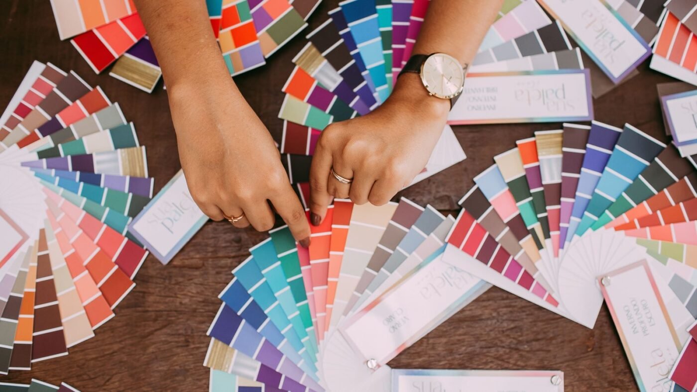 Designer's hands comparing colorful fabric and paint swatches spread across a table