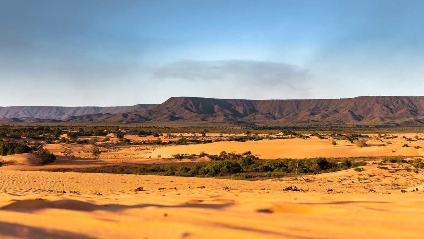 Vast desert sand dunes with distant mountains under a blue sky