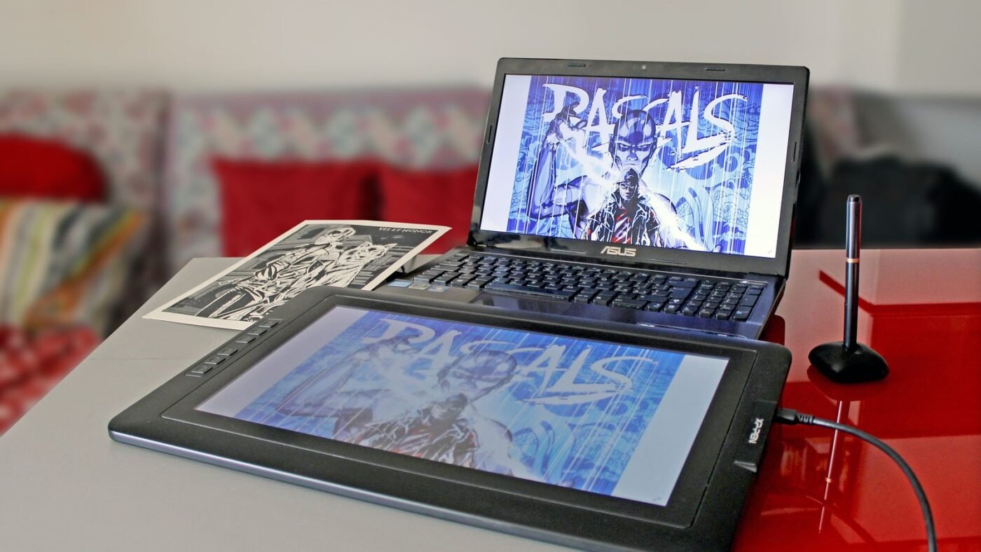 Digital artwork open on a pen display and a laptop at a designer's desk