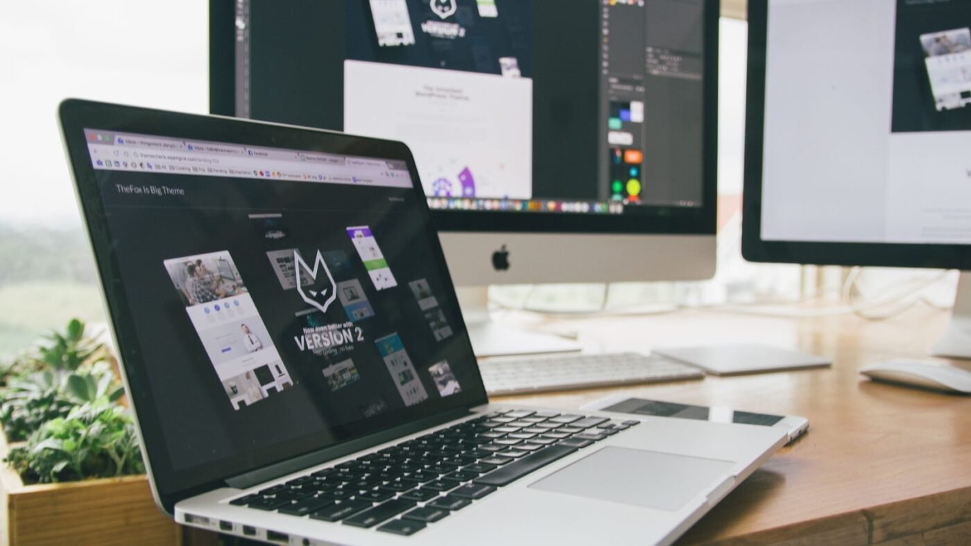 Designer workspace with a laptop and monitors showing design software