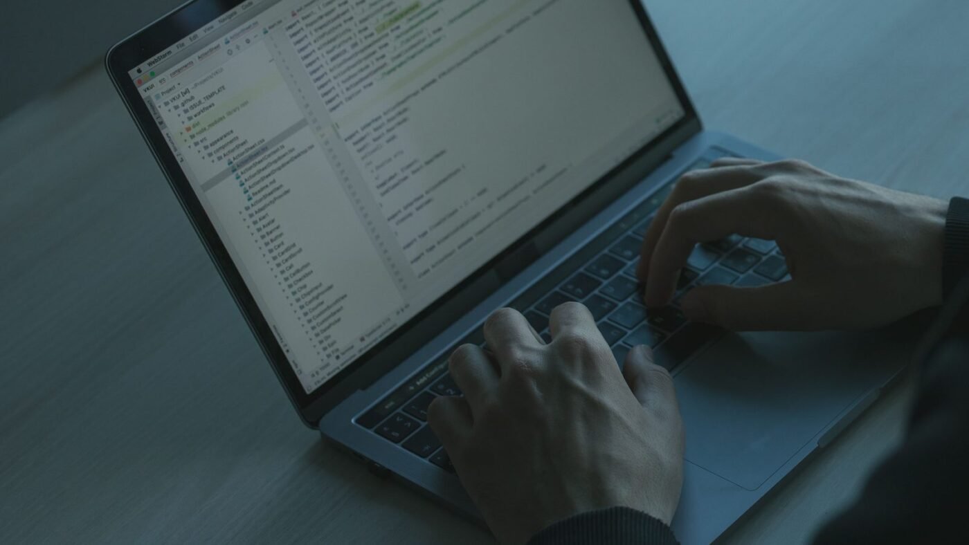 Hands typing on a laptop showing lines of code in a dark room