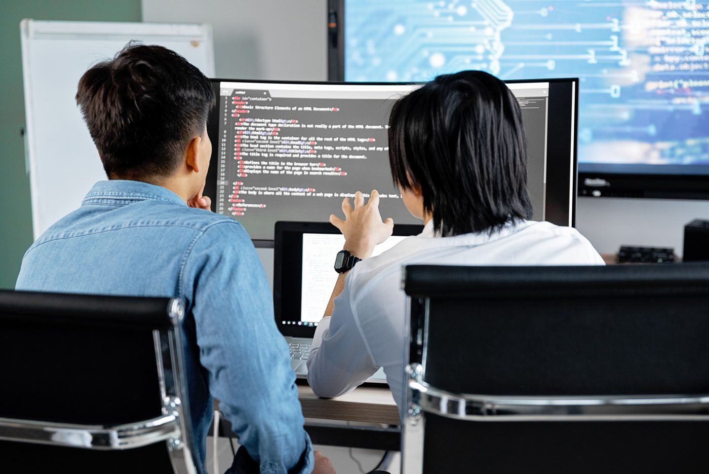 Two developers working at computers with code on their screens in an office