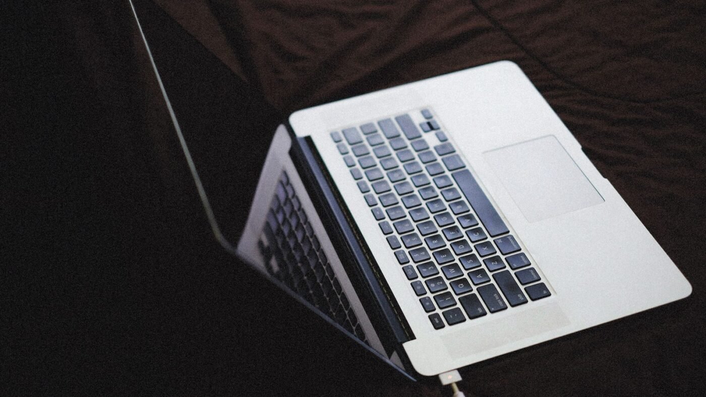Open laptop plugged into a charging cable on a dark surface