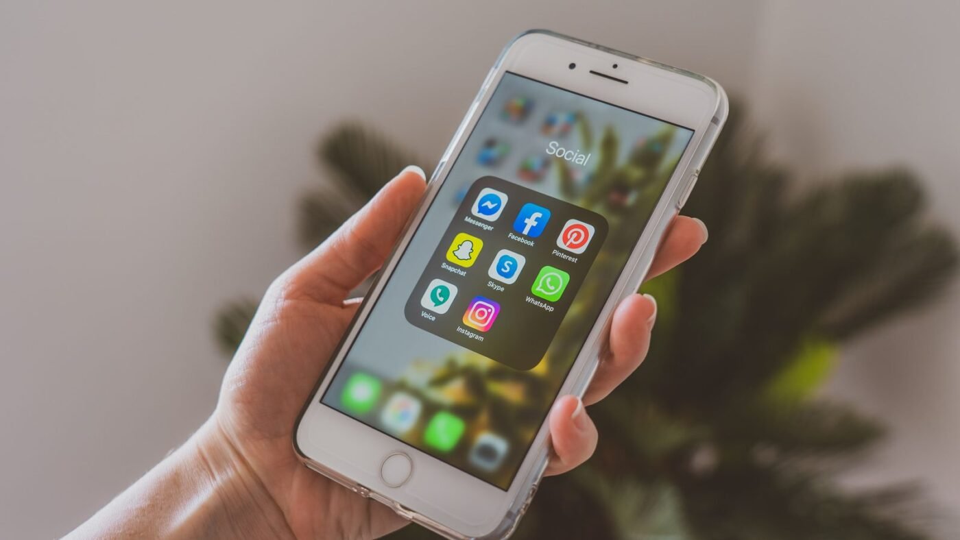 Hand holding an iPhone showing home screen apps