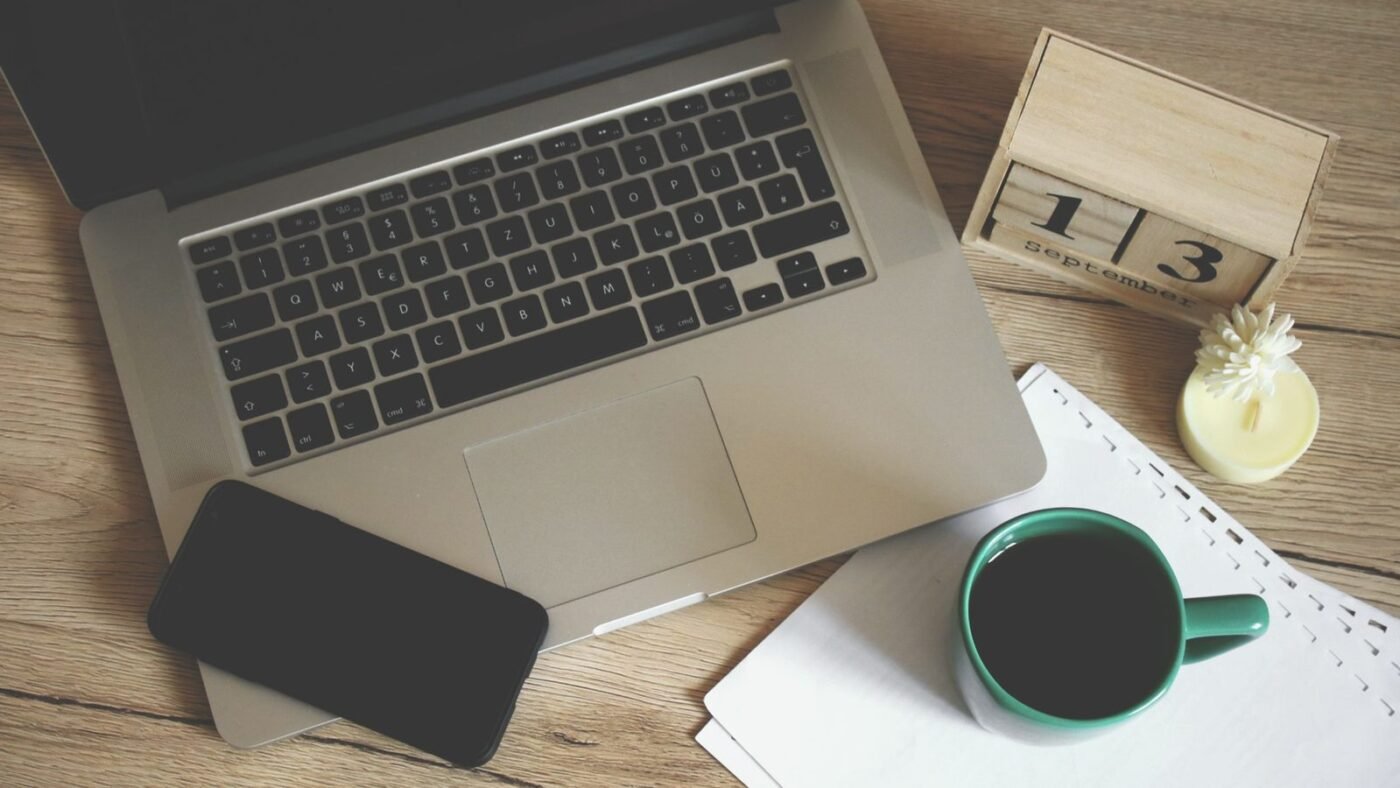 Laptop, smartphone, desk calendar and coffee mug on a wooden desk