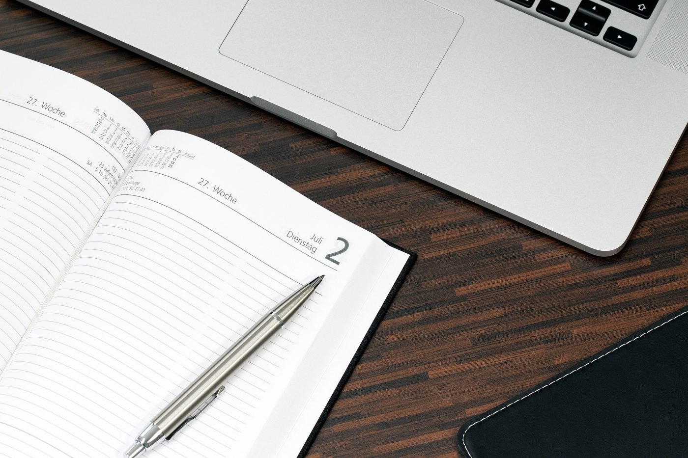 Open daily planner with a pen beside a laptop