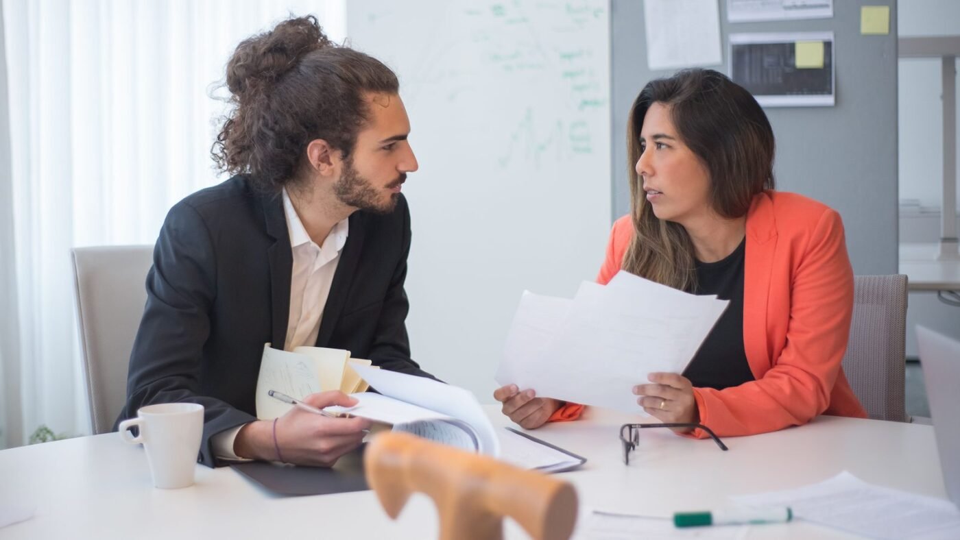 Two colleagues discussing documents across an office table with coffee cups