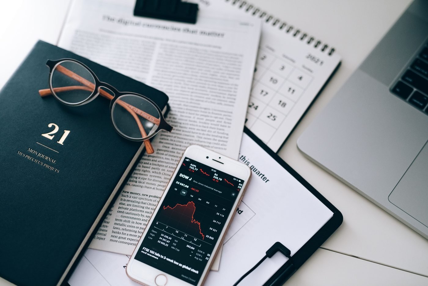 Workspace with financial documents, glasses, a smartphone showing stock data and a laptop