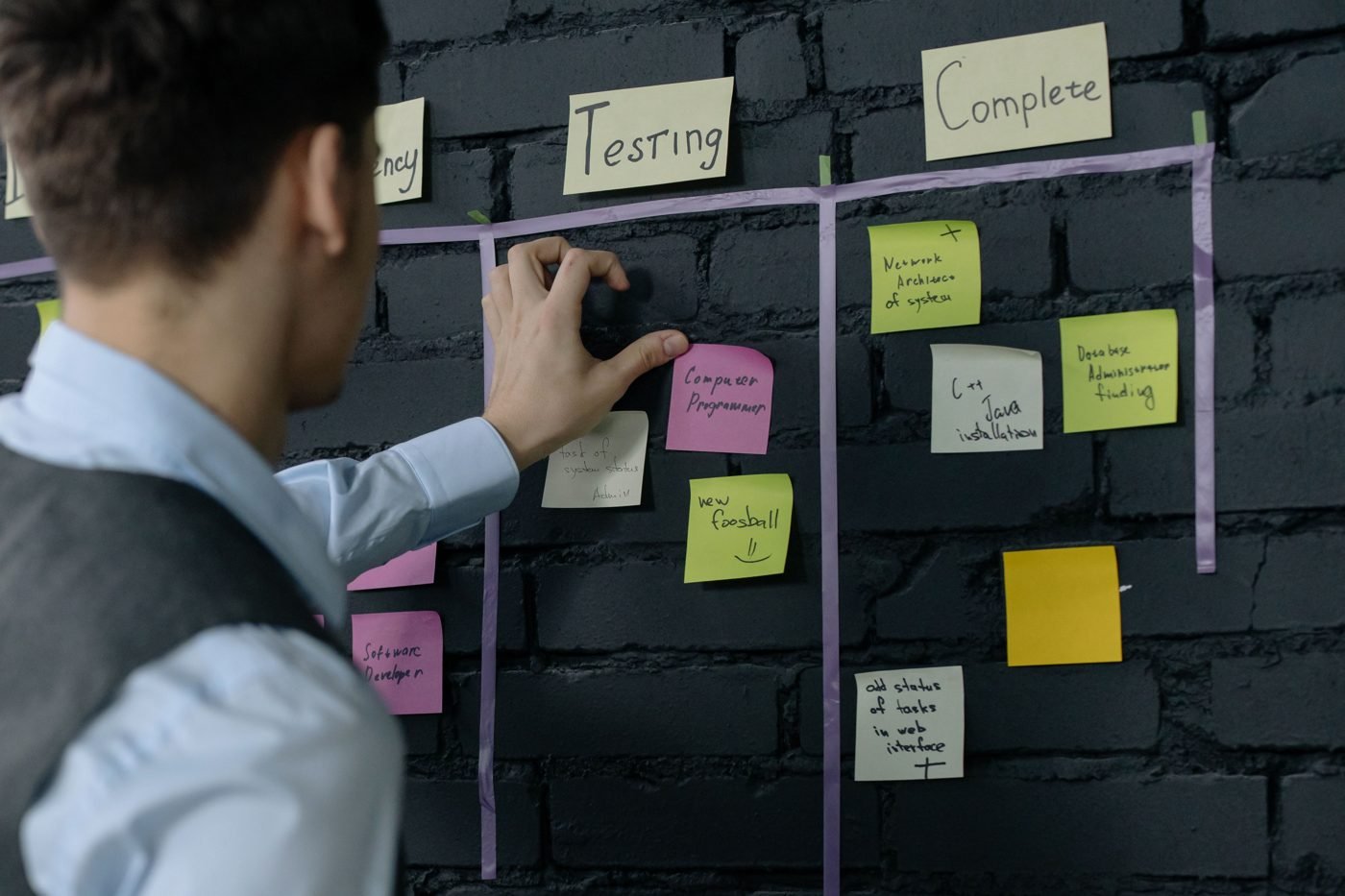 Man moving sticky notes on a kanban board on a dark wall