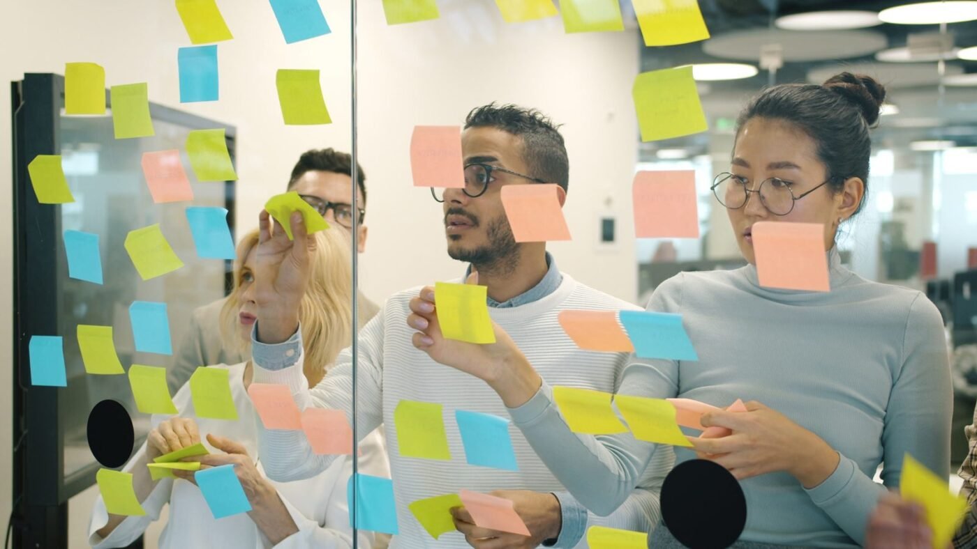 Team members placing colorful sticky notes on a glass wall