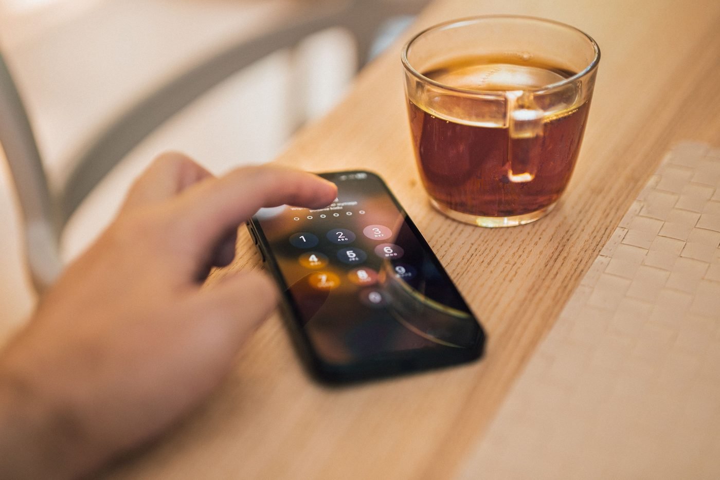 Person unlocking a smartphone next to a cup of tea on a wooden table