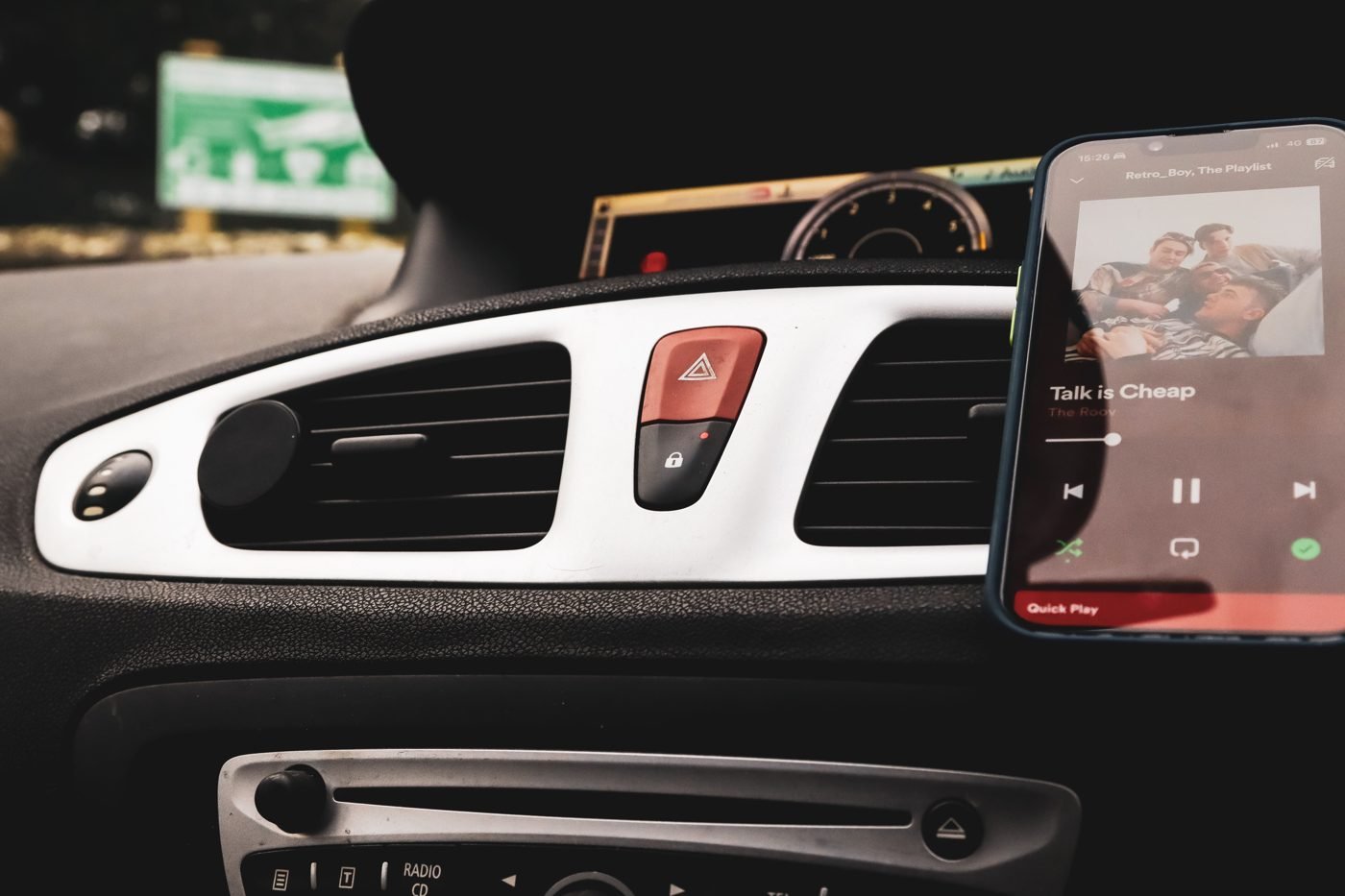 Smartphone playing Spotify mounted in a car next to the dashboard controls