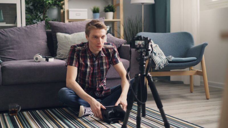 Young man sitting on the floor filming himself with a camera on a tripod