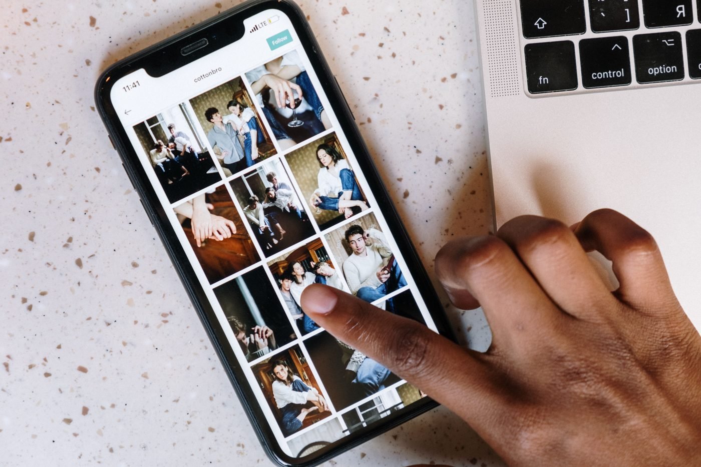 Person browsing photos on a smartphone next to a laptop