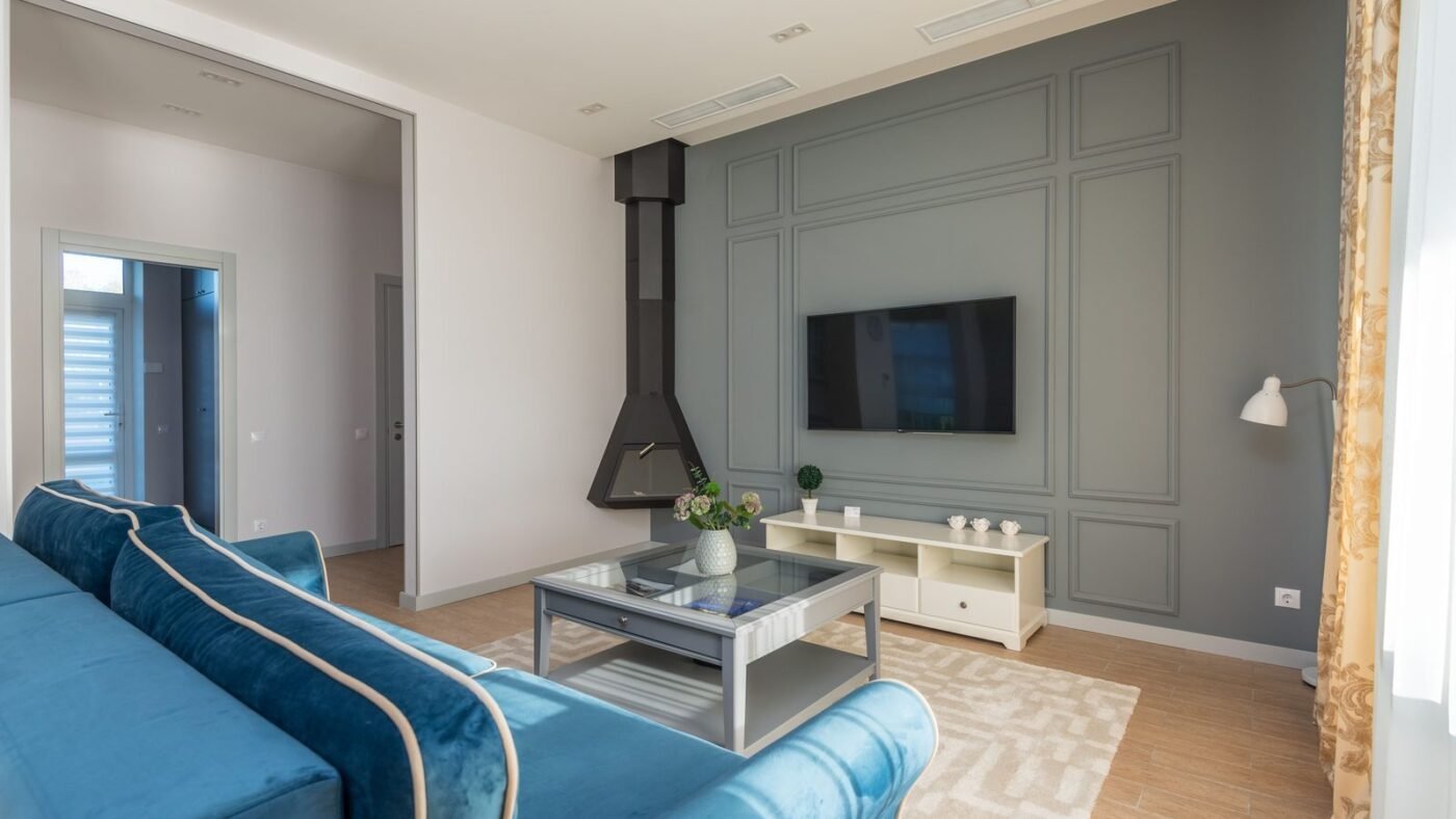 Bright modern living room with a blue sofa, grey paneled wall and wall-mounted TV