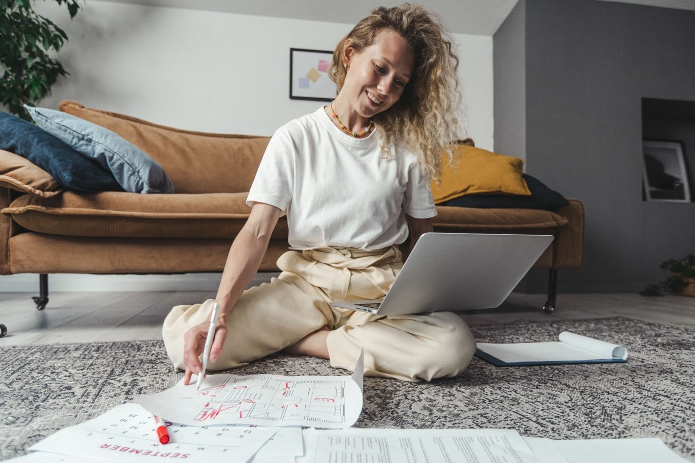 Woman sitting on a living room floor with a laptop and papers, planning a home makeover