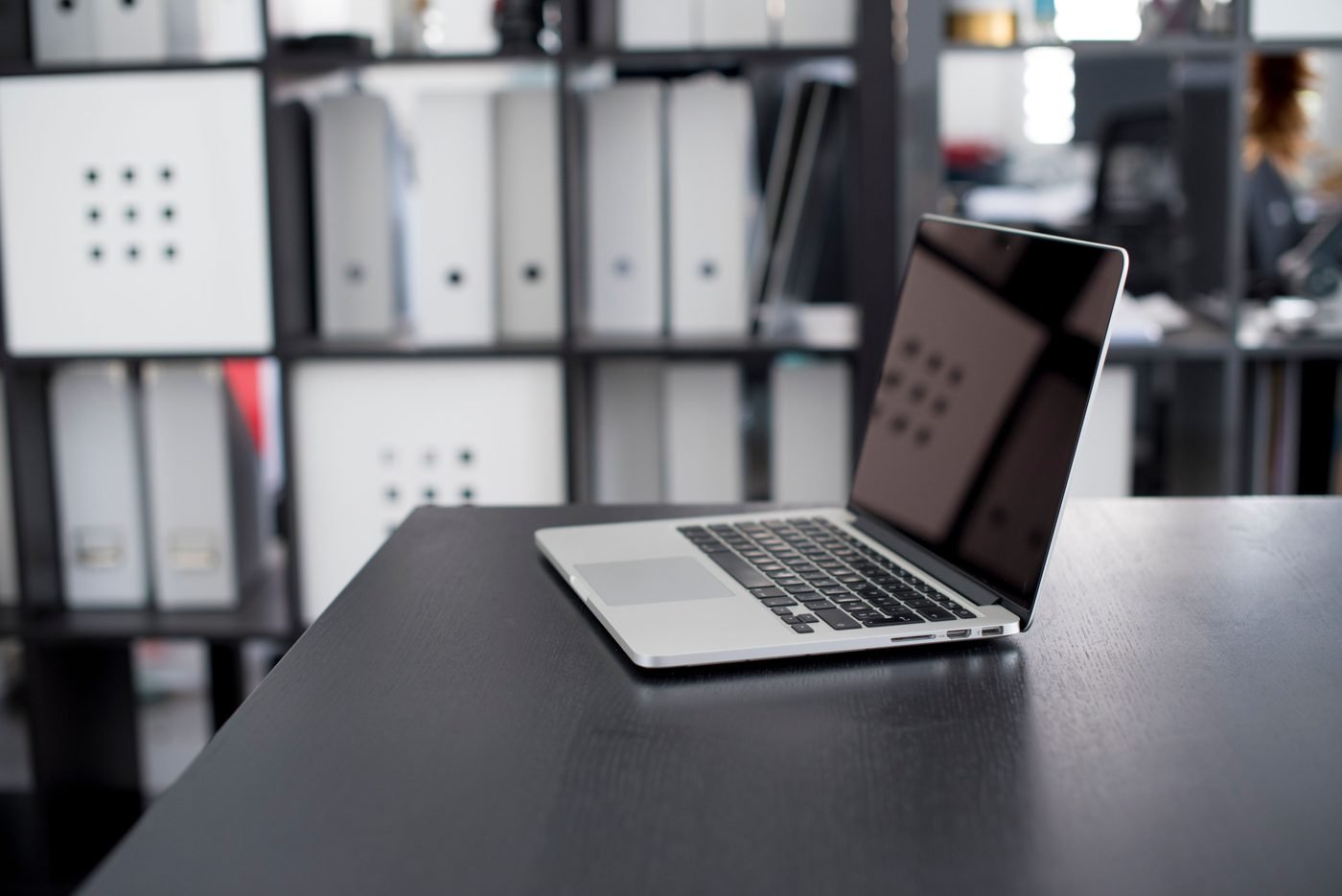 Laptop on a minimalist office desk with shelves of folders behind it