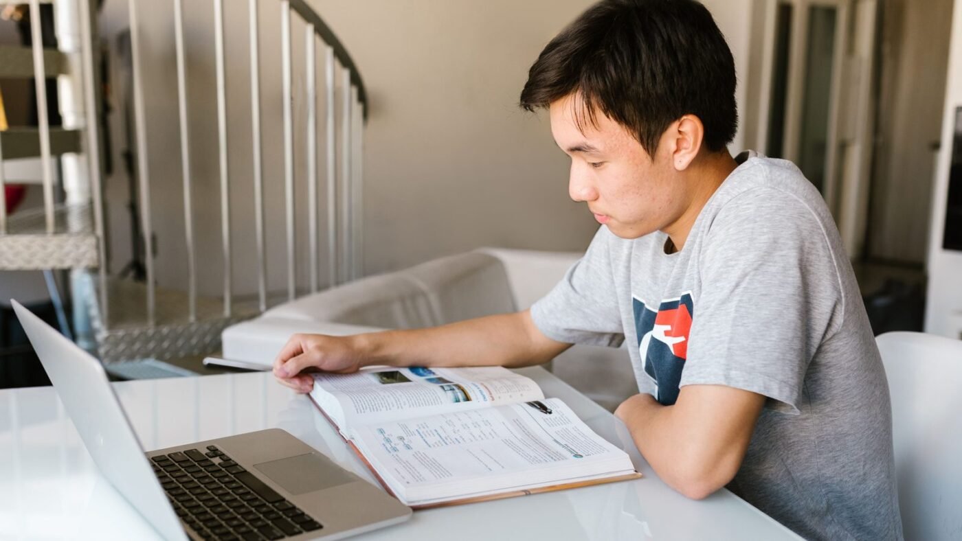 Student studying at a desk with a laptop and an open textbook