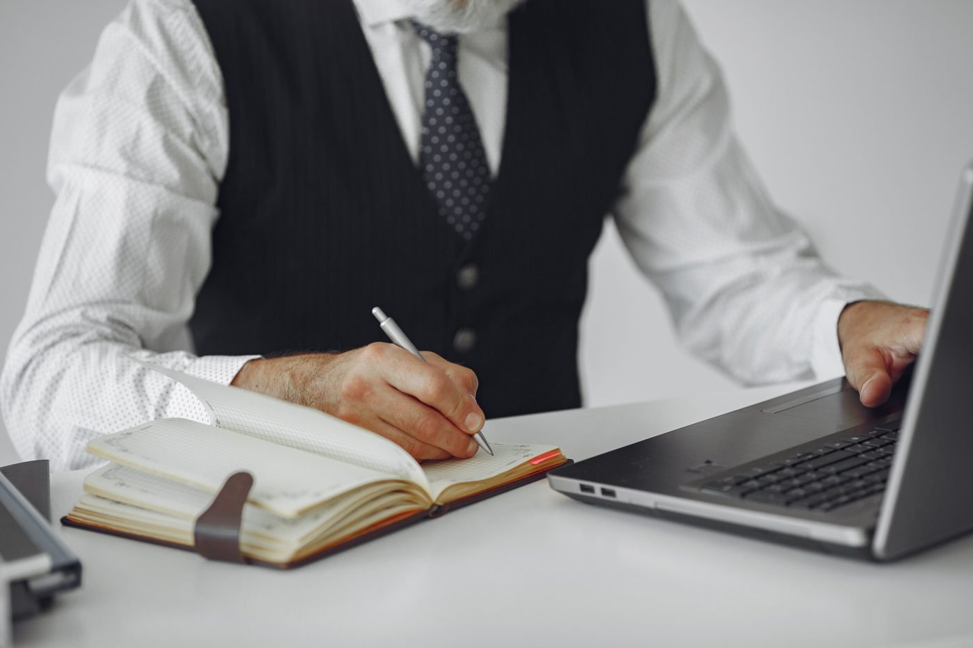Person writing notes in a notebook beside a laptop