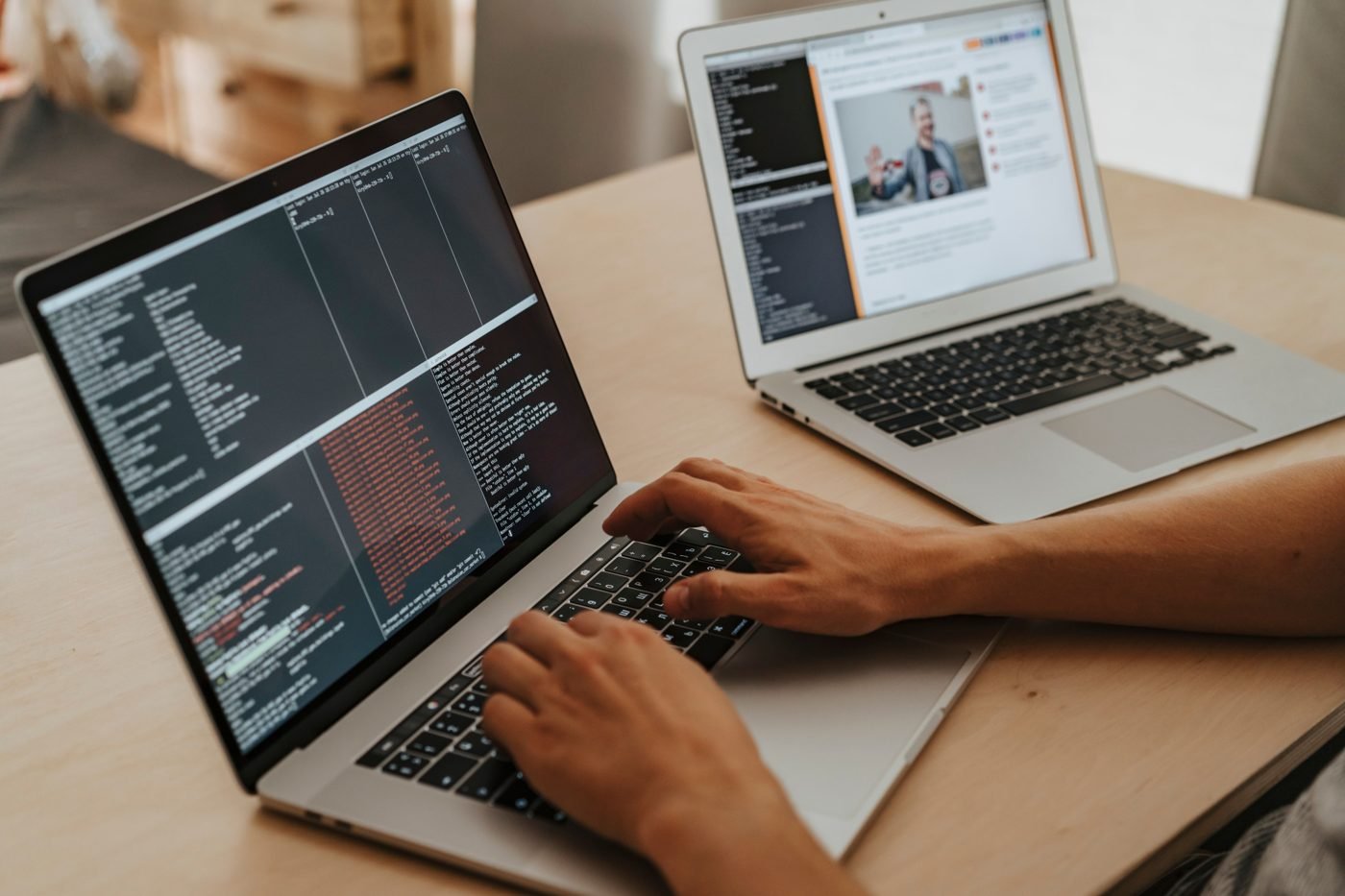 Developer typing code on a laptop with a second laptop beside it