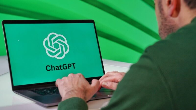 Person typing on a laptop showing the ChatGPT logo on a bright green screen