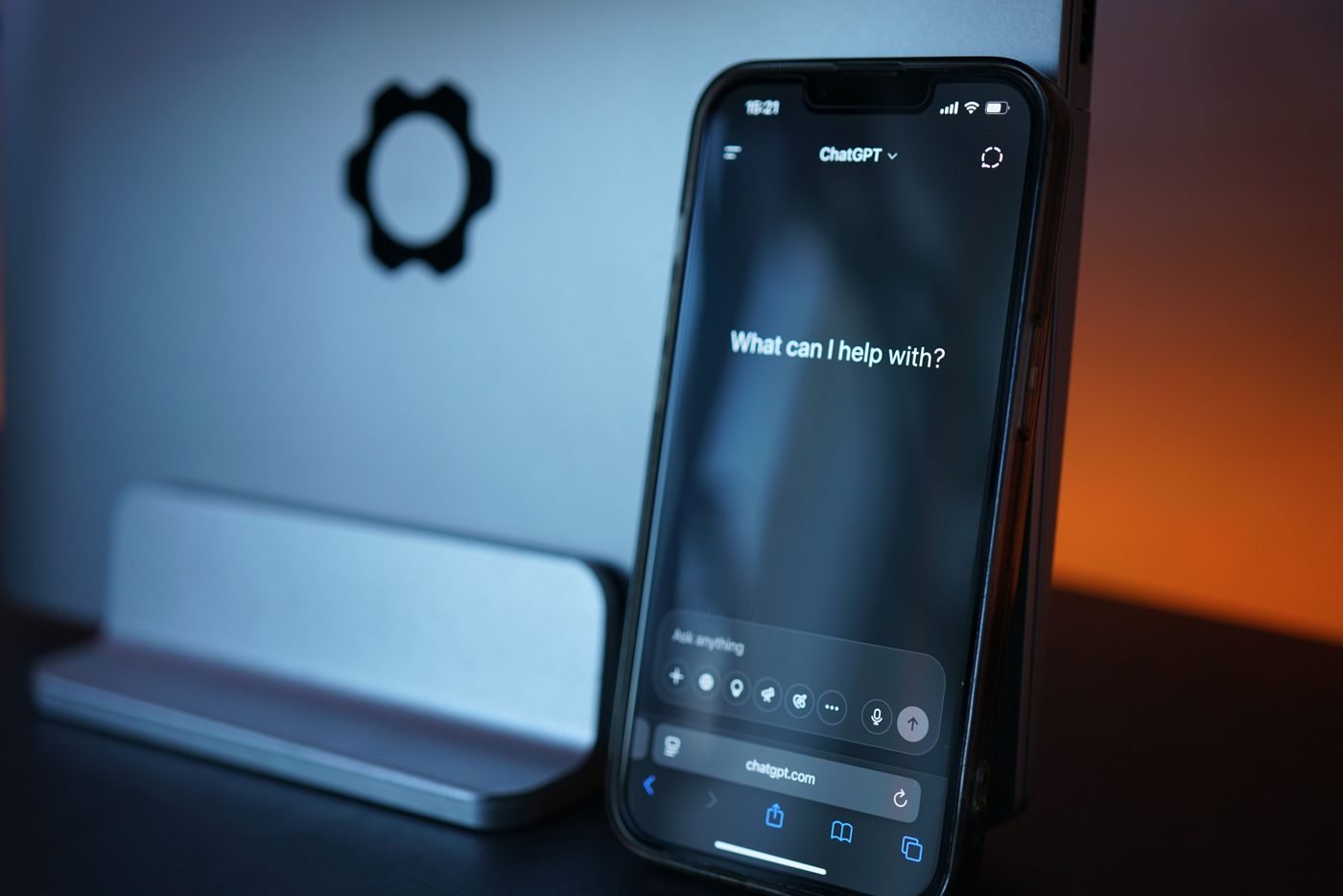 Smartphone on a desk showing an AI chat app asking What can I help with