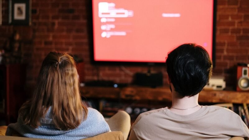 Two people on a sofa watching a large TV in a brick-walled living room