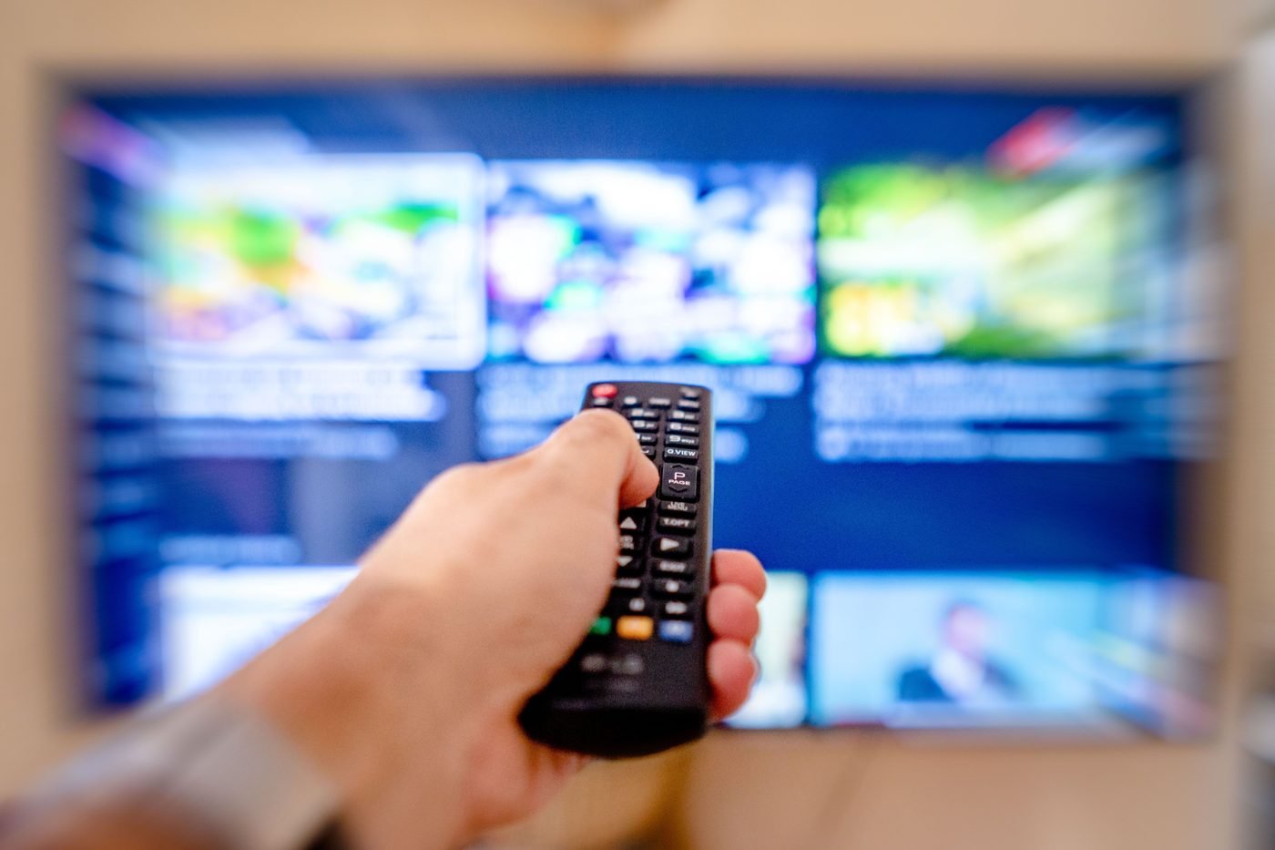 Hand pointing a remote at a TV showing a streaming app menu