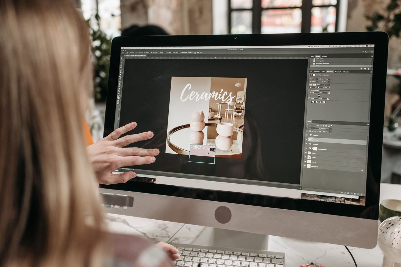 Graphic designer editing a promotional layout in Photoshop on an iMac