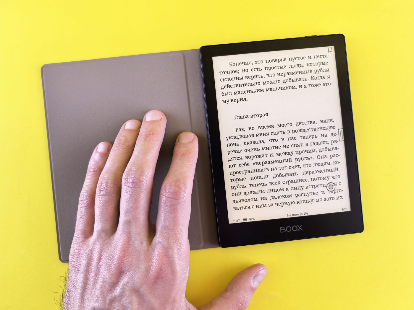 Hand holding an e-reader displaying text against a yellow background