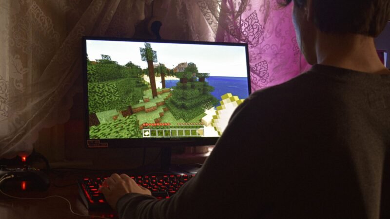 Young man playing a video game on a desktop PC in a dark room